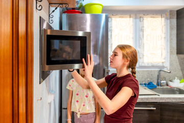 Sisters using microwave oven in home kitchen