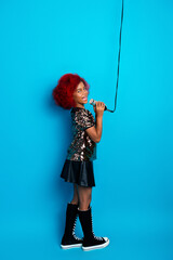 Young girl singer with red hair performs in a blue studio wearing a sequined top and tall boots