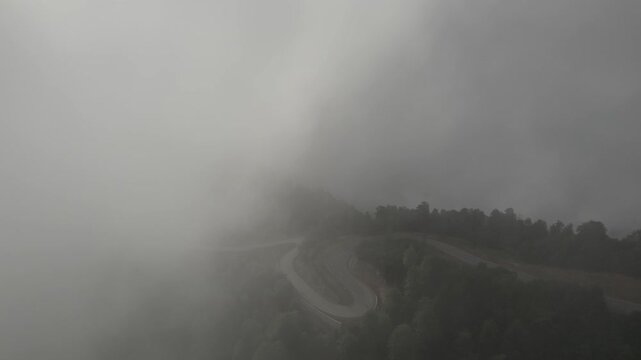 Aerial shot approaching a serpentine mountain road with cars winding through clouds along dramatic curves in the Guria region, Gomis Mta, Georgia