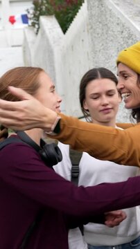 Group of happy female students meeting and embracing on the stairs outside their school building, carrying backpacks and books before class, with a french flag visible in the background