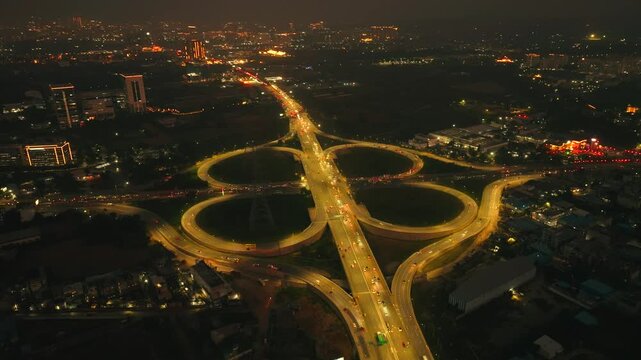 Aerial view of the illuminated Gurugram Deli Expressway cloverleaf interchange with cars zipping at night, Haryana, India.