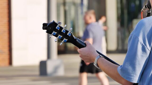 Street musician playing guitar, busking outdoors in Moscow city under sunlight