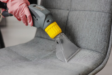 Close up of professional cleaner providing deep cleaning of a fabric chair using vacuum cleaner....