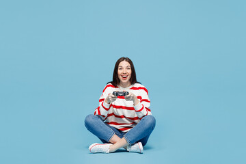 Full body young woman wear red striped sweatshirt casual clothes sit hold in hand play pc game with joystick console isolated on plain pastel light blue background studio portrait. Lifestyle concept. © ViDi Studio