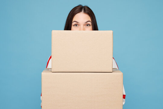 Young woman she wear red striped sweatshirt casual clothes hold cover mouth with stack of two blank cardboard boxes isolated on plain pastel light blue background studio portrait. Lifestyle concept.