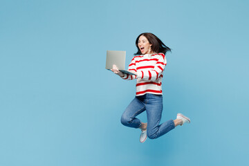 Full body young IT woman she wears red striped sweatshirt casual clothes jump high hold use work on laptop pc computer isolated on plain pastel light blue background studio portrait Lifestyle concept