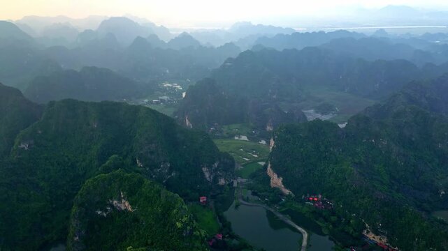 Aerial view of dramatic limestone karsts rising from emerald rice paddies and serene lakes, creating a breathtaking landscape, Hoa Lu, Ninh Binh, Vietnam.