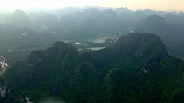 Aerial view of dramatic, lush green mountains, a beautiful landscape dotted with water bodies and shrouded in a gentle haze, Hoa Lu, Ninh Binh, Vietnam.