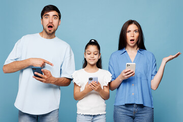 Young shocked parents mom dad with child kid daughter girl wearing casual clothes hold in hand use...