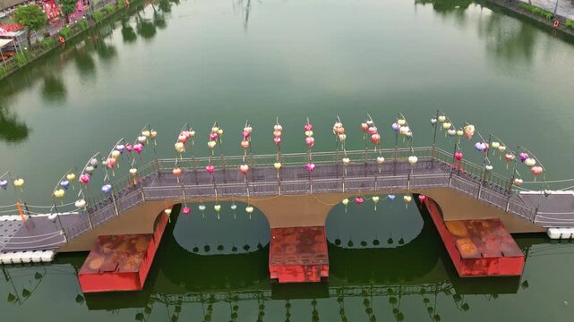 Aerial view of a bridge adorned with colorful lanterns reflected in the still, dark green water, a tranquil scene, Hoa Lu, Ninh Binh, Vietnam.