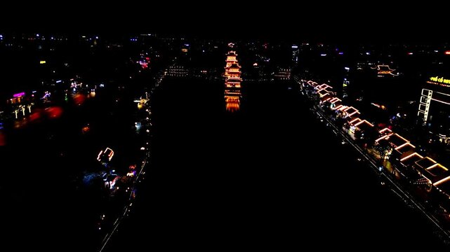 Aerial view of the pagoda and surrounding buildings illuminated with warm lights reflecting in the dark water creating a stunning visual contrast, Hoa Lu, Ninh Binh, Vietnam.