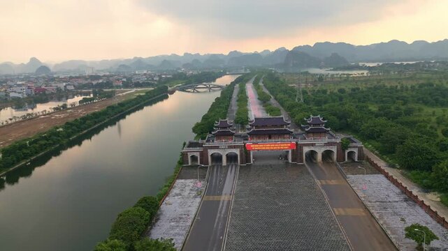 Aerial view of a traditional gate along a river, with the city melding into the distant mountains, creating a striking contrast of urban and natural landscapes, Hoa Lu, Ninh Binh, Vietnam.
