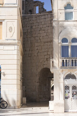 Two simple, square windows with white frames set into a weathered, rustic stone and plaster wall of an old European building under a terracotta roof. © Impresyjna
