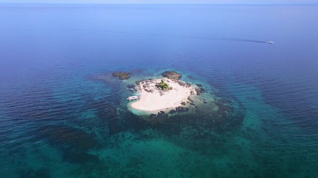 Aerial view of a small island with white sand, boats, and clear turquoise water, contrasting against the deep blue sea, Carles, Western Visayas, Philippines.