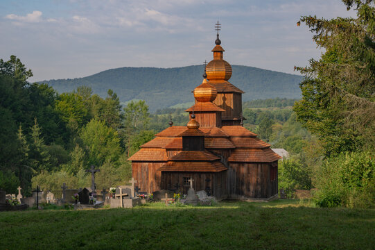 View of the rustic wooden church with its copper domes gleaming warmly under the sun, amidst the verdant landscape, Dobroslava, Presov Region, Slovakia.