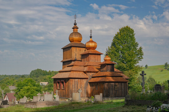 View of a rustic wooden church stands bathed in the warm glow of the setting sun, casting long shadows across the old cemetery, Wooden Church of St. Parascheva, Presov Region, Slovakia.