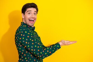 Happy man in green shirt with tiny prints presents products against bright yellow background