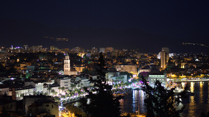 A breathtaking night view of Split, Croatia, with the city lights and the illuminated Saint Domnius bell tower reflecting in the dark Adriatic Sea.