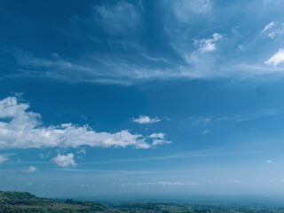 Beautiful aerial view of terraced vegetable plantations on a lush mountain slope under a bright blue sky with white clouds.