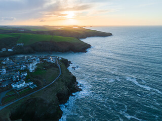 Aerial view of the coastline with houses perched on the cliff edge where the dark blue sea meets the land under a golden sunset sky, Salcombe, England, United Kingdom.