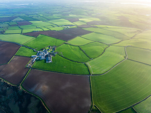 Aerial view of patchwork fields stitched together in vibrant greens and earthy browns, punctuated by a central farmstead, Salcombe, England, United Kingdom.