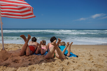 Relaxing by the sea, family lies on beach under striped umbrella