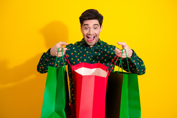 Happy young man shops with colorful gift bags in a bright yellow studio