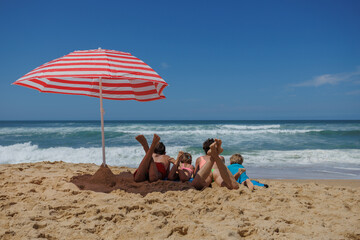 Family of four lies on sandy beach, enjoy the ocean at sunny day