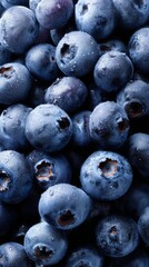 A cluster of fresh blueberries sits against a soft, solid light background. Their deep blue skin shimmers with tiny droplets, hinting at freshness and deliciousness.