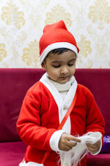 cute baby santa posing with beard on red sofa indoors