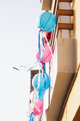 Colorful paper lanterns hang from a balcony during a festive celebration on a sunny day