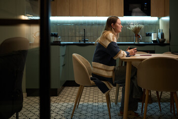 Woman sitting in profile at kitchen table with coffee mug