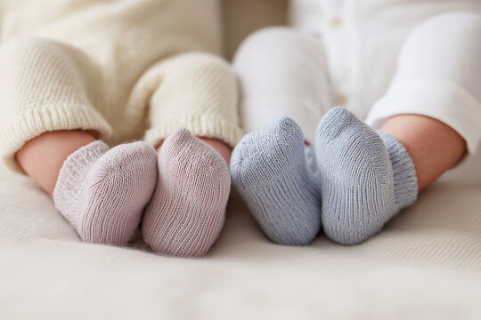 Babies wearing soft socks sit on a light-colored surface beside each other in a cozy space