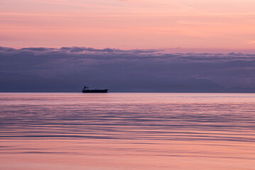 View of the silhouette of a ship cuts a lonely figure on the tranquil, rose-tinted waters beneath a lavender sky, Oak Harbor, Washington, United States.