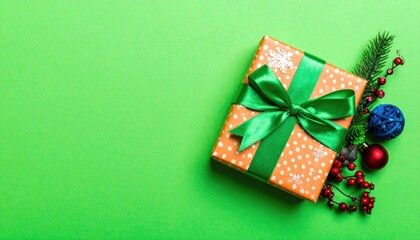 Brightly wrapped Christmas gift box with festive ornaments and pine sprig on green background.