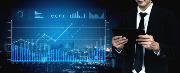 A businessman in a formal suit uses a tablet to analyze financial data, surrounded by modern digital graphs and charts in a city office at night, emphasizing insight and professional growth. Scalp
