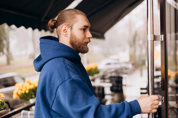 Young man wearing a blue hoodie smiling while opening a cafe door. © sav_an_dreas
