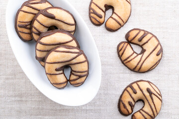 Crescent shaped shortbread cookies, in a white bowl on linen. Crumbly biscuits, made from high ratio of butter, along with sugar and flour, glazed with chocolate, chocolate dipped at the bottom. Photo