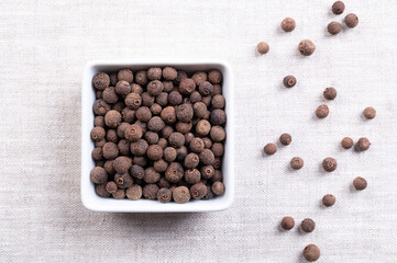 Whole allspice berries, in white bowl on linen. Jamaica pepper, myrtle pepper, and pimento, a spice, combining flavors of cinnamon, nutmeg and clove. Dried unripe berry fruits of Pimenta dioica. Photo