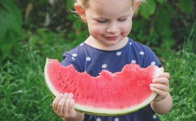 Happy little girl eating a big piece of juicy watermelon against the background of a green garden