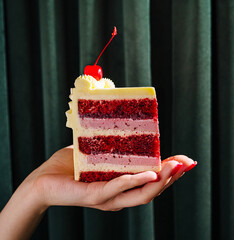Delicious multicolored cake served with a cherry on top held in a hand