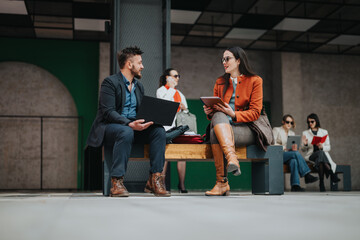 Two coworkers sit on a bench, laptops and notebooks in hand, sharing ideas. In the background, friends read and talk, creating a collaborative, lively office or campus vibe.
