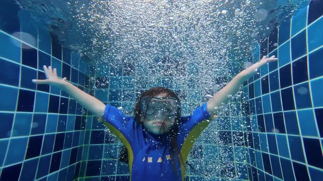Kid dropping into swimming pool with bubbles surrounding in slow motion