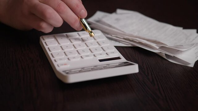 Hand With Pen On Calculator And Receipts, Accountant Using Fountain Pen To Indicate Totals, Pile Of Receipts And White Calculator On Dark Desk, Deliberate Audit And Verification Action