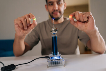 Bearded student male demonstrating mini tesla coil generating wireless power, excitingly lighting up small light bulbs through electromagnetic induction, experimenting with electricity and physics.