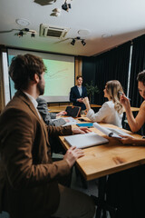 A presenter speaks to colleagues in a conference room with a projecting chart, while teammates review documents, take notes, and share ideas during a collaborative business meeting.