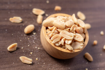 Peanuts in a wooden cup rest on a natural wood floor, creating a warm and rustic food-themed scene.