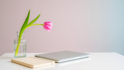 Elegant workspace featuring a laptop, a notebook, and a vibrant pink tulip in a vase, creating a serene atmosphere in a modern setting