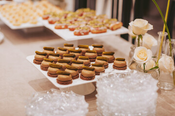 Small plates hold various desserts arranged neatly. There are sweet treats topped with green and brown layers. Soft flowers are in small vases nearby, adding a touch of decor