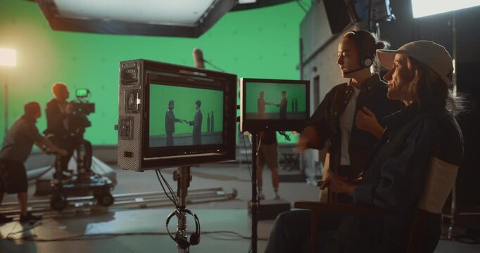 Director and Assistant Review Live Playback on Monitors While Crew Operates Camera Dolly, Filming Tense Action Scene With Large Green Screen for Visual Special Effect